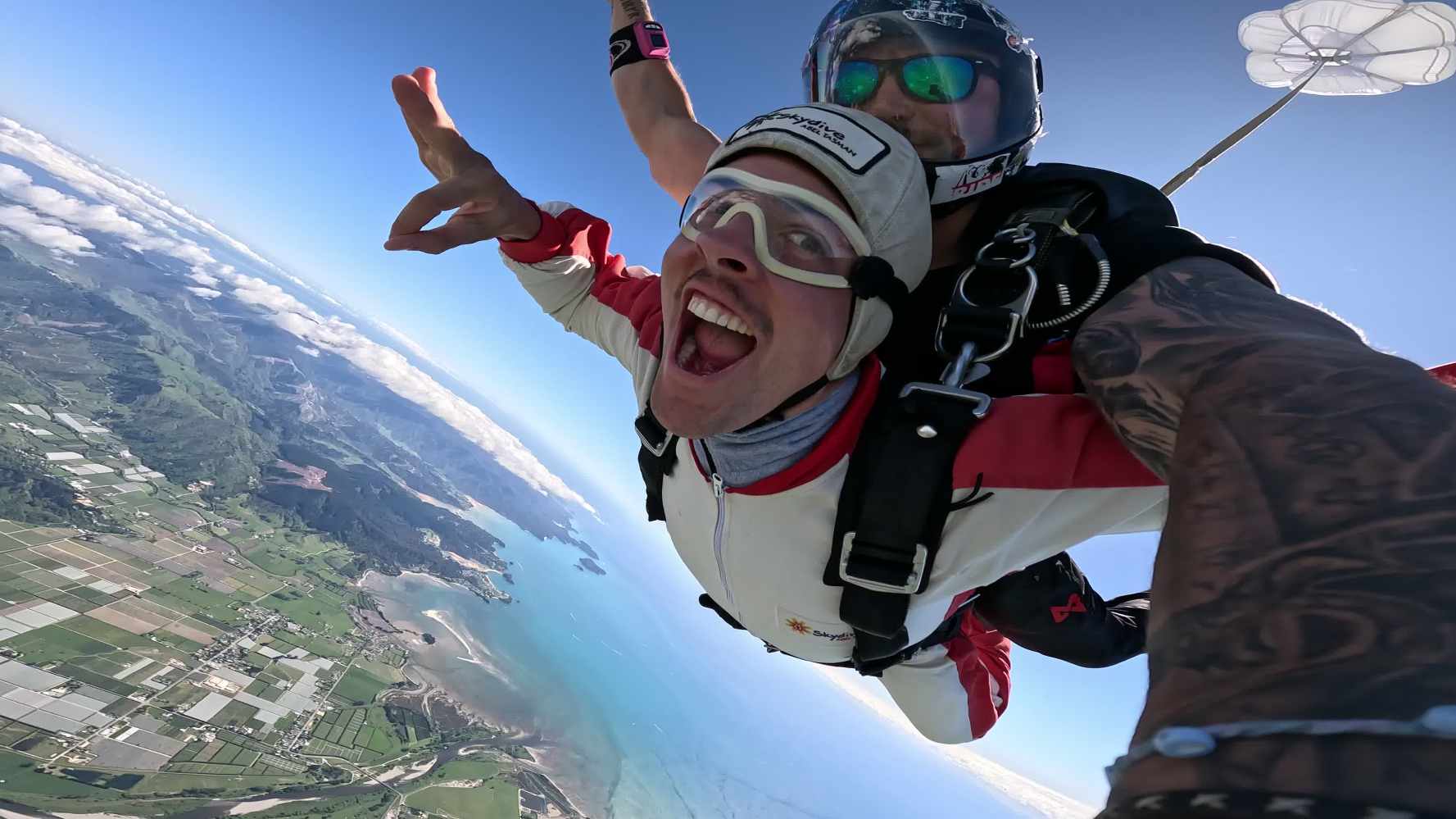 Tandem skydivers in teh air with crazy facial expression